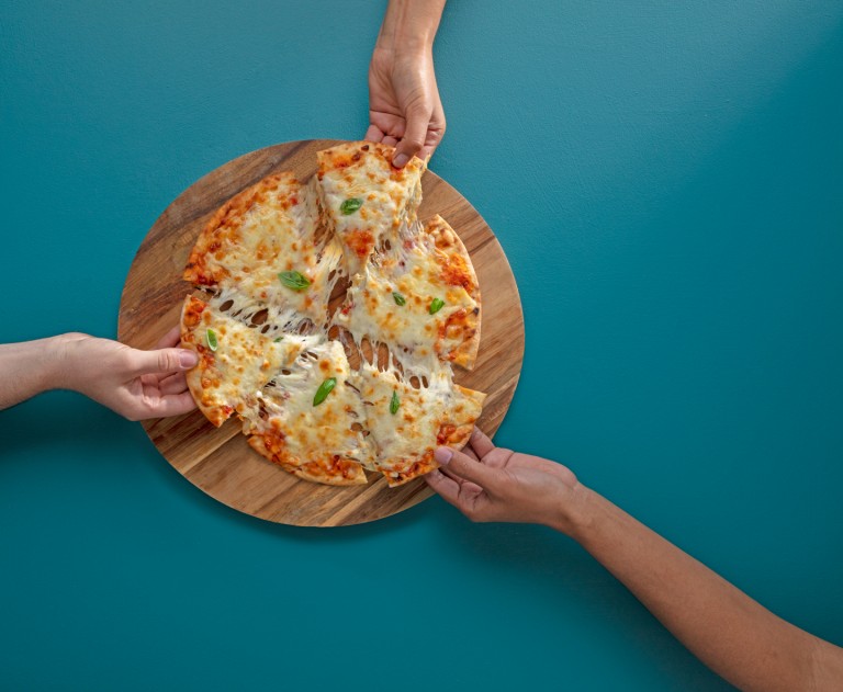 Three hands taking slices of cheese pizza from a board